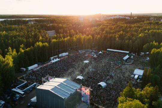 Ilmakuva Provinssista, päälavan yläpuolelta. Aurinko paistaa, paljon asiakkaita ja Provinssin myyntipisteitä, taustalla vehreää metsää ja rakennuksia.