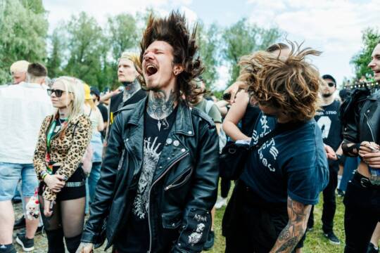 Heviteemalla pukeutuneita ihmisiä yleisössä heiluttamassa hiuksia.