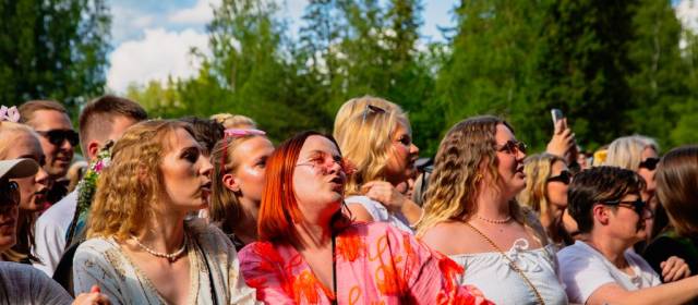 Värikkäästi pukeutuneita iloisia ihmisiä eturivissä.