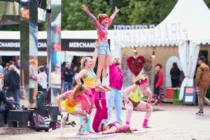 Sirkus Muudin ihmispyramidi. Esiintyjillä on päällä värikkäät pinkin, keltaisen ja sinisen sävyiset asut.